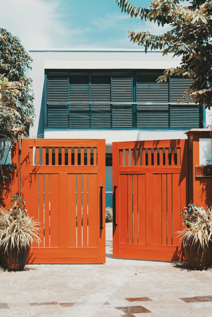 Stylish wooden gates open to reveal a modern villa facade, surrounded by lush tropical plants.